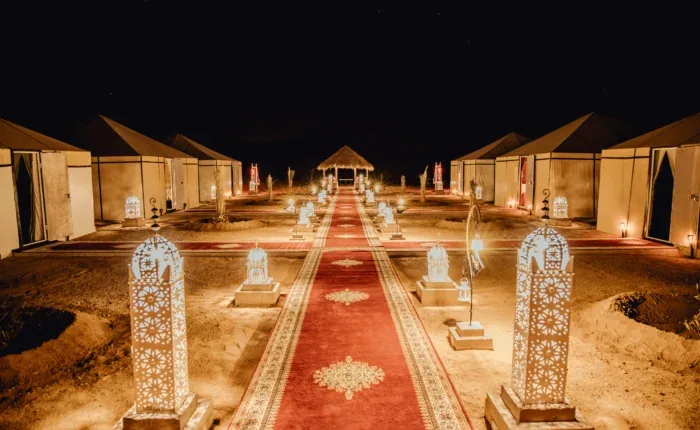 Illuminated desert camp tents beside a patterned walkway at night