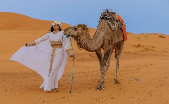 Traveler standing beside a camel in orange desert dunes